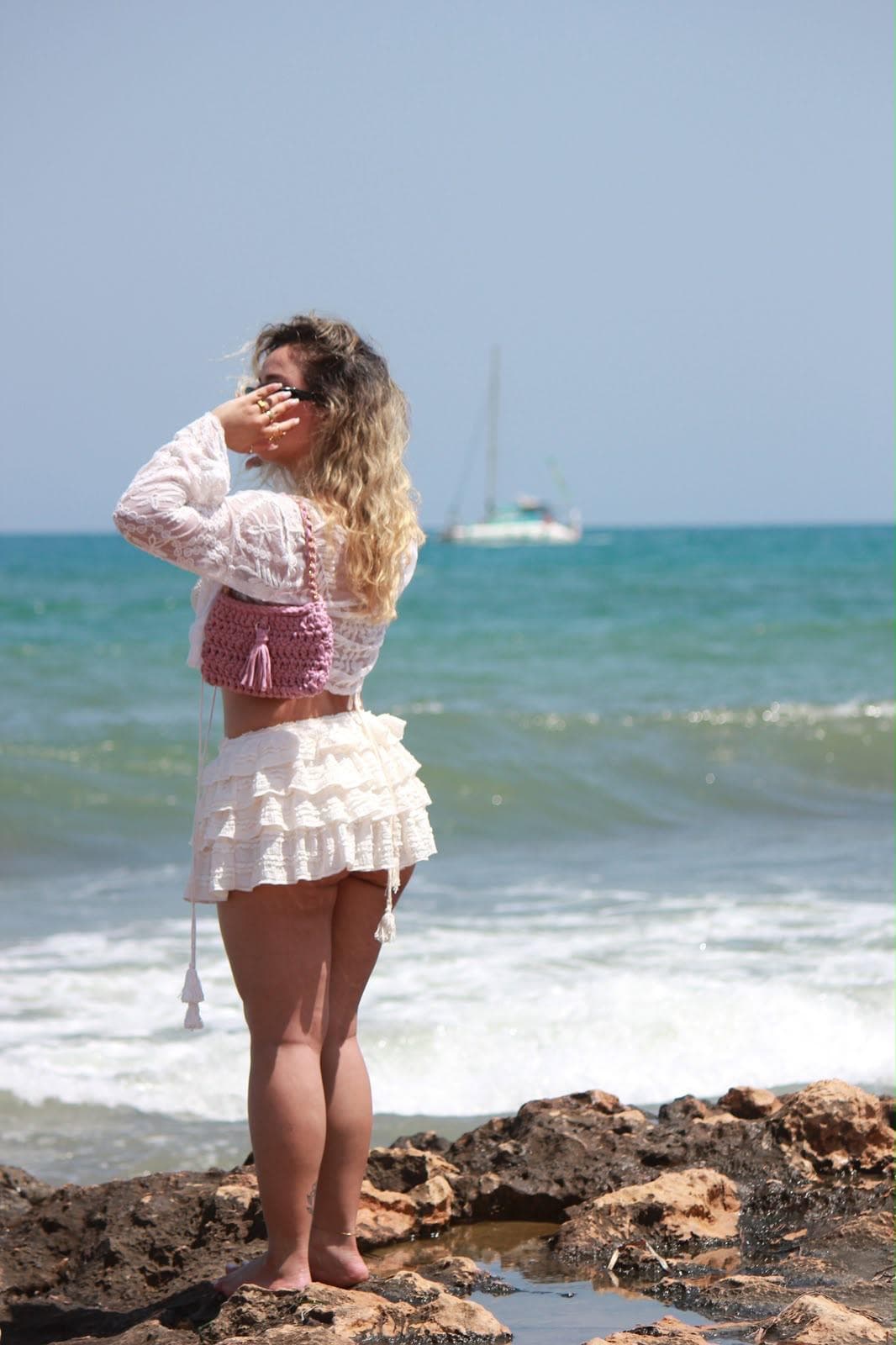 Nairy Zoghbe de espaldas frente al mar con un bolso de crochet rosa con borla, hecho a mano — ZoghBrand